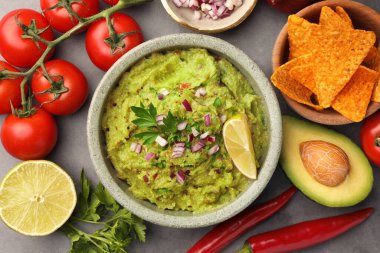 Bir kase lezzetli guacamole, cips ve malzemeler gri masada, düz yerde.