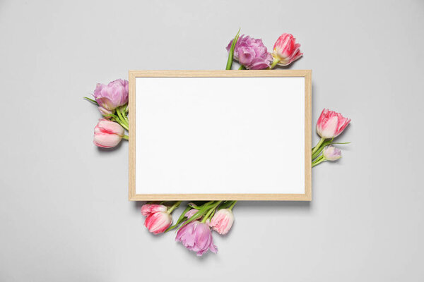 Empty photo frame and beautiful flowers on light gray background, top view. Space for design