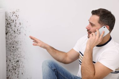 Küf temizleme servisi. Telefonda konuşan ve etkilenmiş duvarlara bakan bir adam.