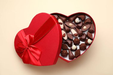 Heart shaped box with delicious chocolate candies on beige background, top view
