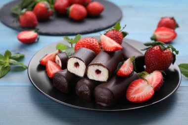 Lezzetli kremalı atıştırmalıklar taze çilekler ve açık mavi ahşap masada nane şekeri.