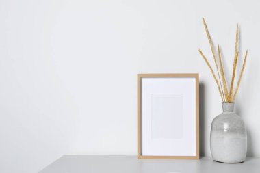 Boş fotoğraf çerçevesi ve vazo. Beyaz masa üzerinde kuru dekoratif çiviler var. Tasarım için model