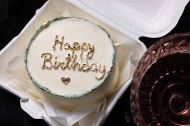 Lezzetli dekore edilmiş doğum günü pastası ve siyah arka planda bir bardak şarap.