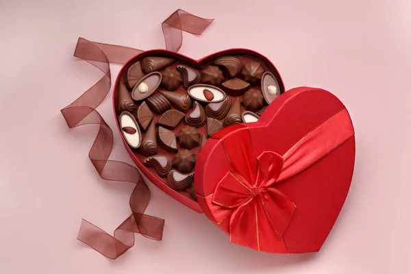 薄いピンクの背景においしいチョコレートキャンディーやリボンとハート型の箱 フラットレイ — ストック写真