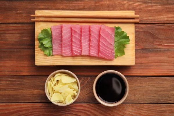 Lezzetli sashimi (taze çiğ ton balığı parçaları), marul, soya sosu ve ahşap masada zencefil dilimleri.