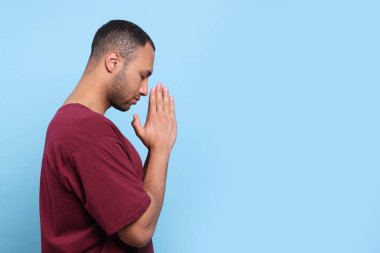 Elleri sımsıkı bağlı Afro-Amerikalı bir adam açık mavi arka planda Tanrı 'ya dua ediyor. Metin için boşluk
