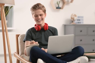 Çevrimiçi öğrenme. Evde dizüstü bilgisayarda yazan gülümseyen genç çocuk.