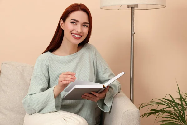 红头发的快乐女人和书本坐在屋里的沙发上 — 图库照片