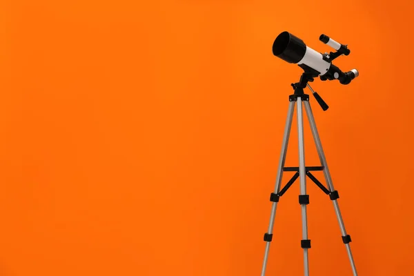 Tripod with modern telescope on orange background. Space for text