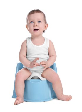 Küçük çocuk beyaz arka planda bebek tuvaletinde oturuyor.