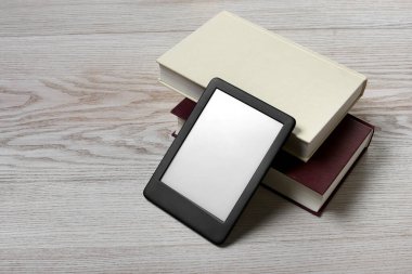 Taşınabilir e-kitap okuyucu ve beyaz ahşap masa üzerindeki ciltli kitaplar