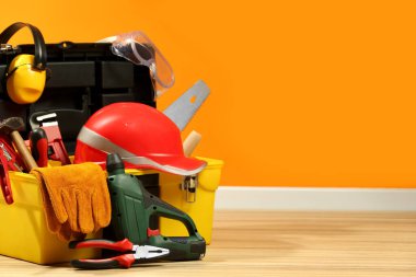 Box with different tools for repair on floor near orange wall, space for text