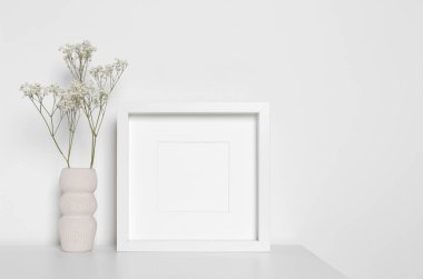 Boş fotoğraf çerçevesi ve vazo, dekoratif çingene çiçekleri beyaz masada. Tasarım için model