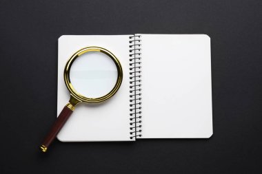 Koyu arkaplanda büyüteç ve defter, üst görünümde