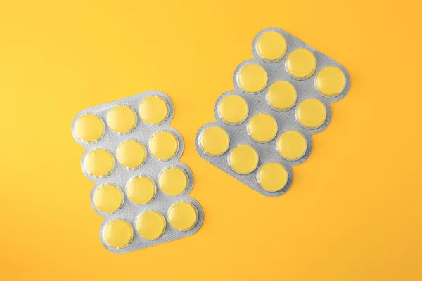 Blisters with cough drops on yellow background, flat lay
