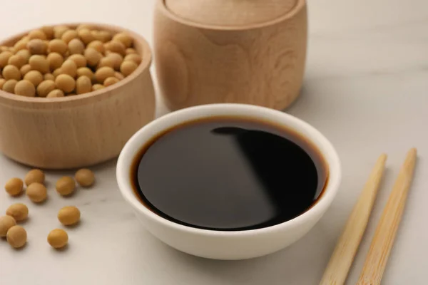 stock image Soy sauce in bowl, soybeans and chopsticks on white table, closeup