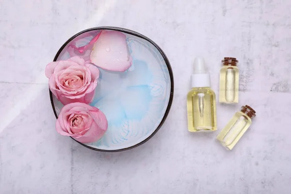 stock image Flat lay composition with bowl of water, flowers and essential oils on light table. Spa treatment