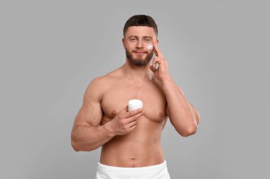 Yakışıklı bir adam açık gri arka planda yüzüne krem sürüyor.