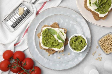 Krem peynirli lezzetli bruschettalar, pesto sosu ve açık gri masada taze fesleğen.