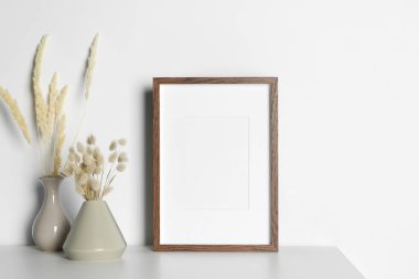 Boş fotoğraf çerçevesi ve beyaz masa üzerinde kuru dekoratif çiviler olan vazolar. Tasarım için model