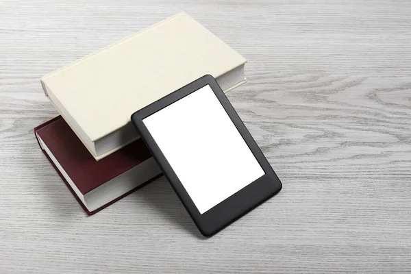 Portable e-book reader and hardcover books on white wooden table