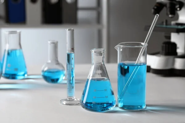 不同的实验室玻璃器皿 桌上有浅蓝色液体 — 图库照片