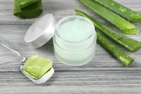 Doğal jöleli kavanoz, soyulmuş aloe vera kaşığı ve açık gri ahşap masada yeşil yapraklar.