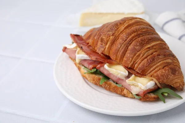 Stock image Tasty croissant with brie cheese, ham and bacon on white tiled table, closeup. Space for text