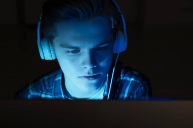 Teenage boy in headphones using computer at night. Internet addiction