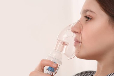 Beyaz arka planda solunum için nebulizör kullanan tatlı bir kız, yakın plan. Metin için boşluk