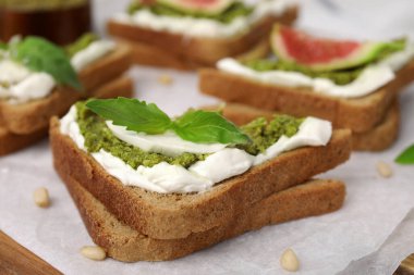 Krem peynirli lezzetli bruschetta, pesto sosu ve parşömen kağıdında taze fesleğen, yakın plan.