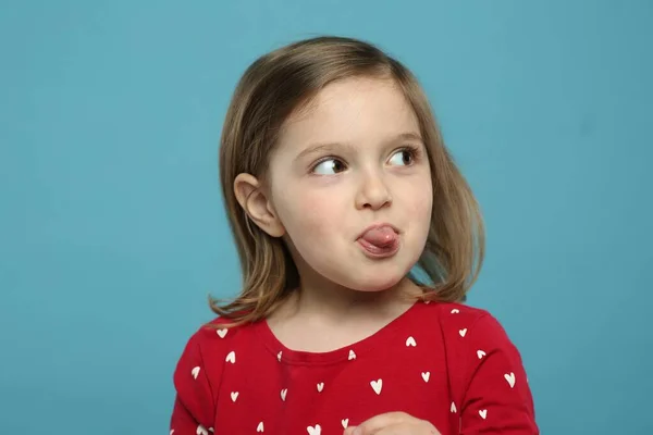 Dilini Açık Mavi Arka Planda Gösteren Komik Küçük Kız — Stok fotoğraf