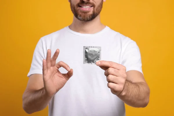 Man Condom Showing Gesture Yellow Background Closeup Safe Sex — Stock Photo, Image