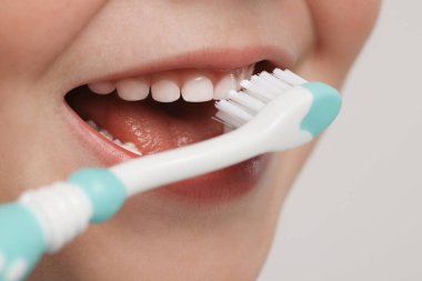 Dişlerini plastik diş fırçasıyla fırçalayan sevimli küçük çocuk açık gri arka planda, yakın plan.
