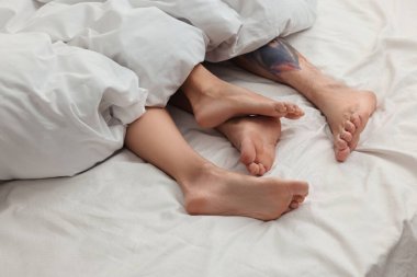 Tutkulu çift yatakta sevişiyor, bacakları birbirine yakın.