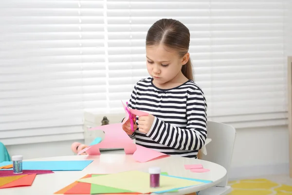 かわいい女の子が部屋の机でピンクの紙を切っている ホームワーク — ストック写真