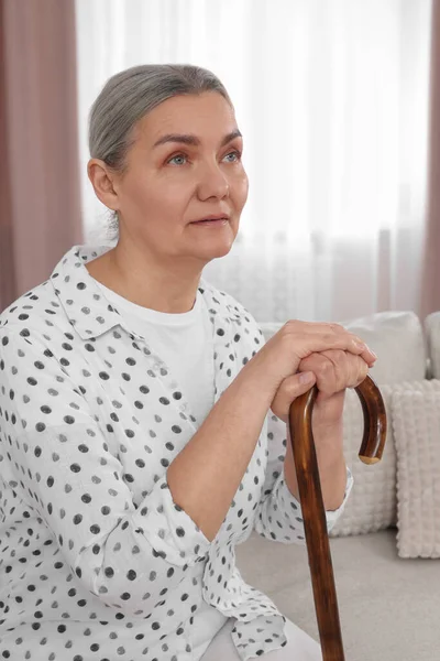 stock image Senior woman with walking cane sitting on sofa at home