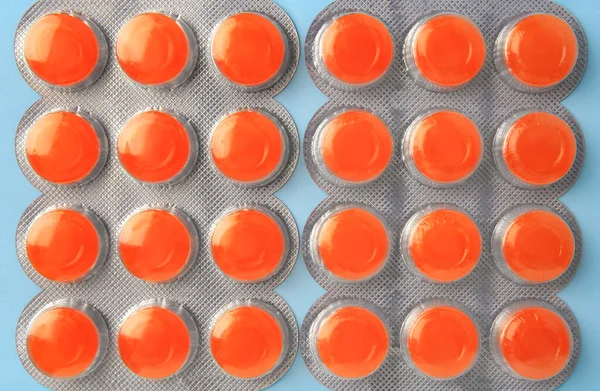 Blisters with orange cough drops on light blue background, flat lay