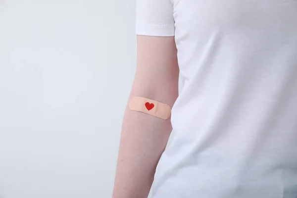 Blood donation concept. Woman with adhesive plaster on arm against white background, closeup. Space for text