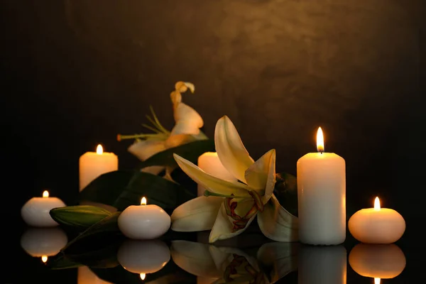 白色的百合花和燃烧的蜡烛在黑暗的黑色镜子表面 文字的空间 丧葬标志 — 图库照片