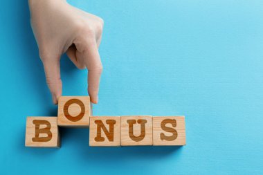 Kadın açık mavi ahşap arka planda harflerle küplerden kelime bonusu yapıyor, üst manzara. Metin için boşluk