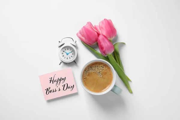 Card with phrase Happy Boss`s Day, coffee, alarm clock and tulips on white table, flat lay