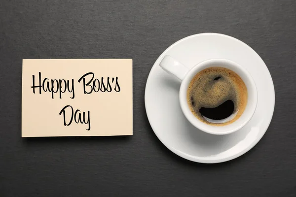 Card with phrase Happy Boss`s Day and cup of coffee on black table, flat lay