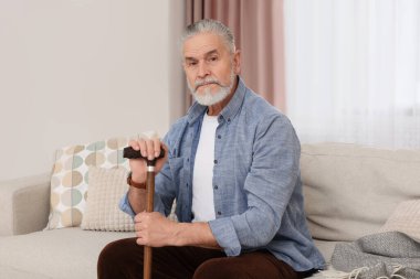 Evdeki kanepede oturan bastonlu yaşlı adam.