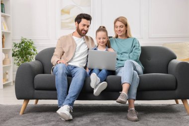 Mutlu aile birlikte vakit geçirip evdeki kanepede dizüstü bilgisayar kullanıyor.