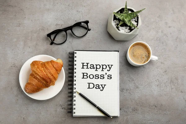 stock image Happy Boss`s Day greeting card. Notebook with phrase, pen, coffee, croissant, glasses and plant on grey table, flat lay