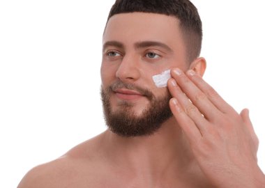 Beyaz arka planda yüzüne krem süren yakışıklı bir adam.