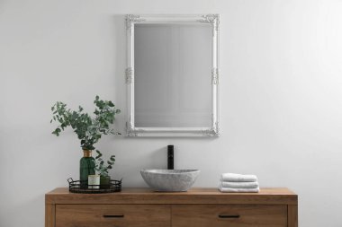 Modern bathroom interior with stylish mirror, eucalyptus branches, vessel sink and wooden vanity