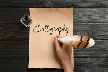 Kelime Hattatlığı yazan kadın, tahta masada tüy ve mürekkeple yazı yazıyor.