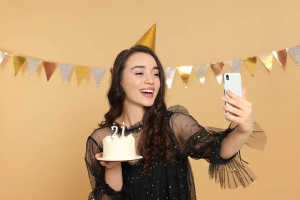 年齢層のパーティー 21歳の誕生日 笑顔の女性保持おいしいケーキとともに番号形のキャンドルと取ります自画自画自画自画自分自身に対してベージュ背景 — ストック写真